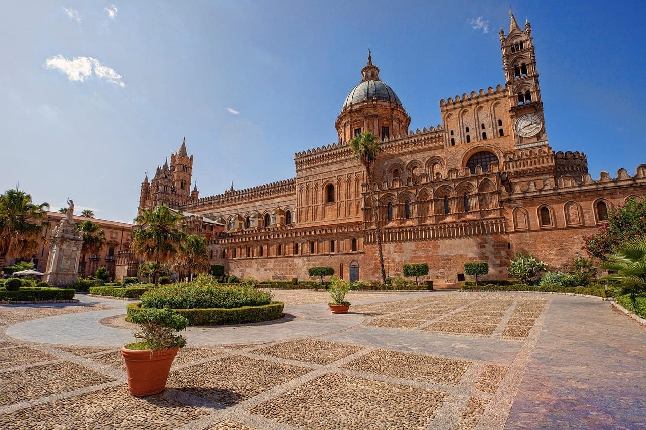 Palermo cathedral with Norman-Arab architecture and palm trees against blue Sicilian sky